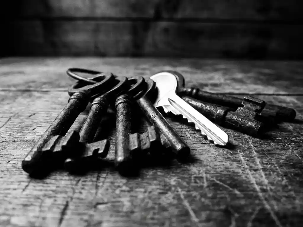 Antike Eisenschlüssel mit Patina auf verwittertem Holztisch, moderner Schlüssel dazwischen, Schwarz-Weiß-Nahaufnahme.